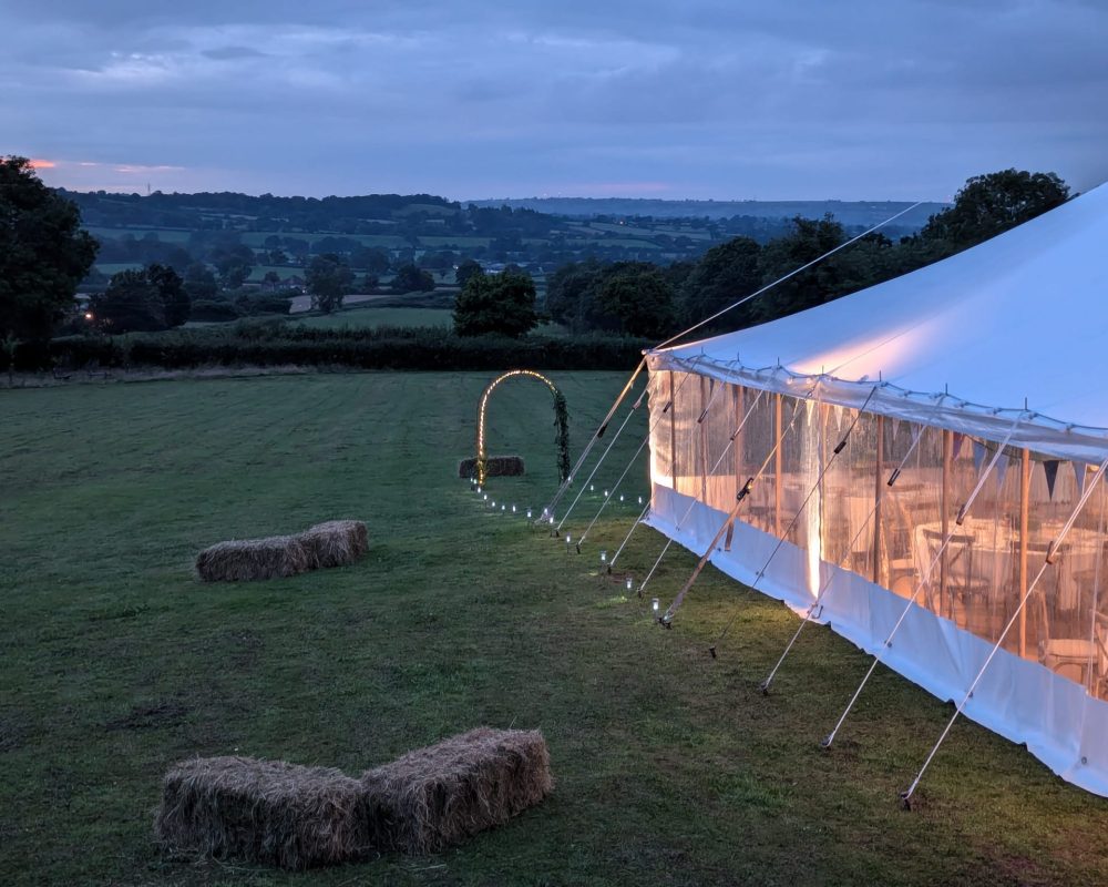 A wedding marquee lit up ready for an evening event. The sun has set, hay bales are in the field.